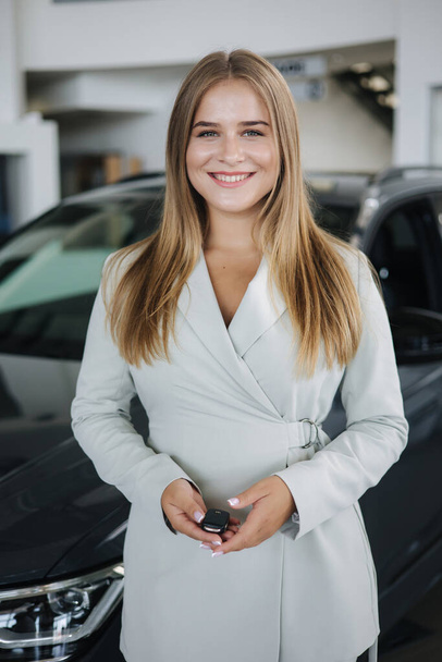 Portrait of beautiful and young business woman in car showroom. Female hold keys from her new car - Photo, Image