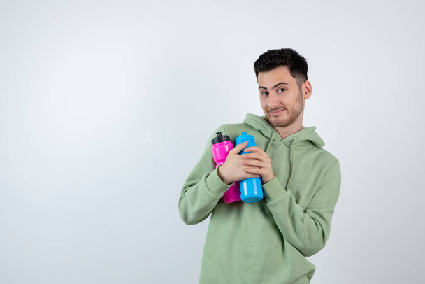 Imagen de un joven barbudo con capucha sosteniendo coloridas botellas de agua. Foto de alta calidad - Foto, Imagen