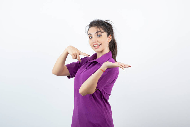 Photo of brunette girl in purple t-shirt standing and pointing. High quality photo - Foto, imagen