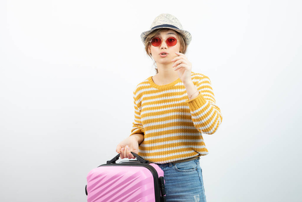 Zdjęcie młodej turystki w kapeluszu trzymającej różową walizkę podróżną. Wysokiej jakości zdjęcie - Zdjęcie, obraz