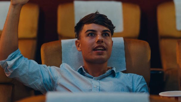 Attractive cheerful young caucasian man laughing while watching film in movie theater. Lifestyle entertainment concept. Close up shot. - Foto, imagen