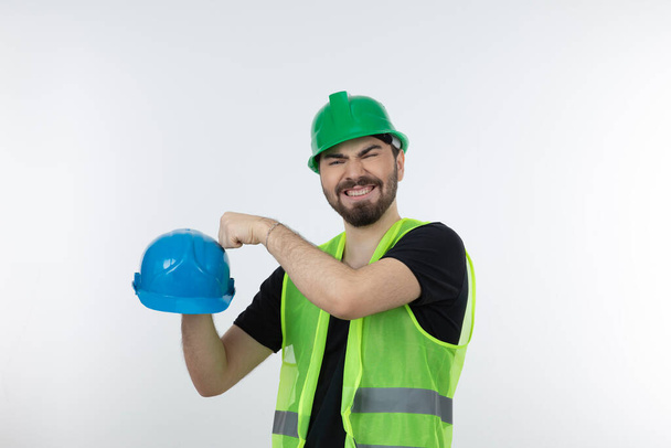 Yeşil yelekli erkek sanayi işçisi kaskını yumruklamaya çalışıyor. Yüksek kalite fotoğraf - Fotoğraf, Görsel