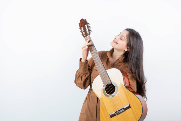 Egy barna nő képe, ahogy gitárt tart a fehér falnak. Kiváló minőségű fénykép - Fotó, kép