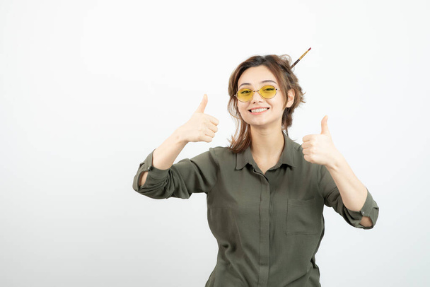 Retrato de menina com coque bagunçado em óculos de pé e dando polegares para cima. Foto de alta qualidade - Foto, Imagem
