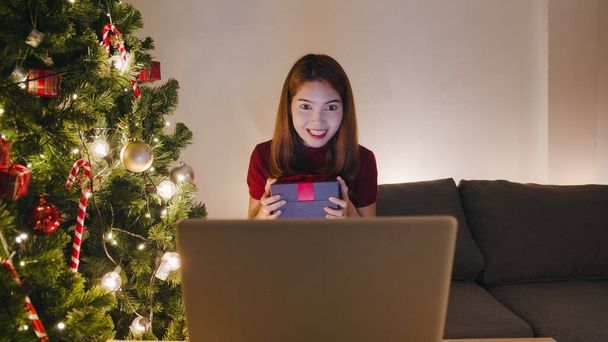 Młoda Azja kobieta za pomocą rozmowy wideo laptopa rozmowy z parą z X 'Mas pudełko prezentów, choinka ozdobiona ozdobą w salonie w domu. Świąteczna noc i święto Nowego Roku. - Zdjęcie, obraz