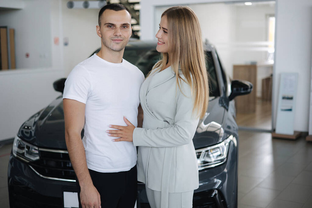 Retrato de hermosa pareja joven feliz después de comprar un coche nuevo en la sala de exposición del coche. Mujer hus su hombre y feliz - Foto, Imagen