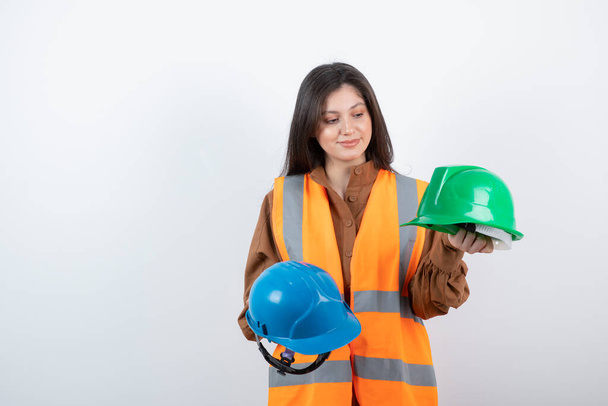 Zdjęcie kobiety inżyniera w kamizelce bezpieczeństwa wybierającej kaski. Wysokiej jakości zdjęcie - Zdjęcie, obraz