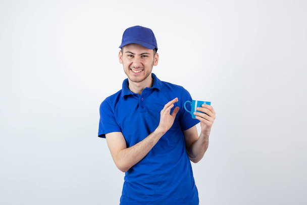 Ένα νεαρό όμορφο αγόρι με μπλε στολή που κρατάει ένα φλιτζάνι τσάι. Υψηλής ποιότητας φωτογραφία - Φωτογραφία, εικόνα