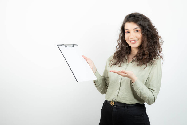 A beautiful young business woman standing and holding clipboard over white wall. High quality photo - Фото, изображение
