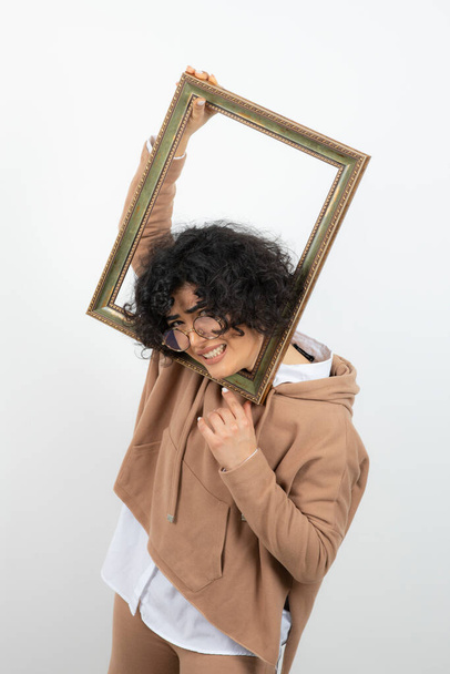 lockige brünette junge Frau lustig posiert mit leerem Bilderrahmen - Foto, Bild