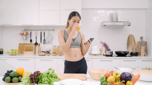 Young Asian blogger woman using smartphone for talking, chatting and checking social media in the kitchen, female in sport clothing cooking at home. Lifestyle women relax at home concept. - Foto, Imagem