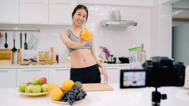 Blogger sporty Asian woman using camera recording how to make orange juice video for her subscriber, female use organic fruit making orange juice by herself at home. Healthy food concept. - Photo, Image