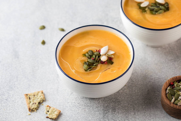 Two bowls with pumpkin cream soup and pumpkin seeds on a gray background. Top view. Autumn recipes. - Φωτογραφία, εικόνα