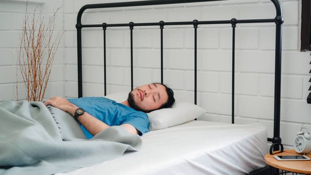Jonge Aziatische man wakker in de ochtend, man stretching na wakker op bed in de slaapkamer thuis. Knappe mannen dutten, slaperig ontspannen in modern huisconcept. - Foto, afbeelding