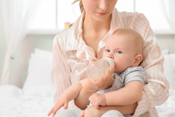 Η νεαρή μητέρα δίνει νερό στο γλυκό μωρό της στην κρεβατοκάμαρα. - Φωτογραφία, εικόνα