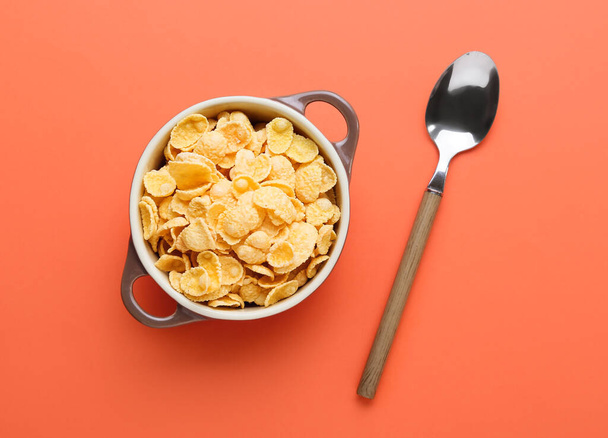 Pot with tasty cornflakes and spoon on color background - Photo, Image