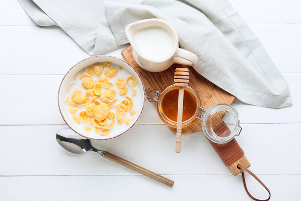 Composition with tasty cornflakes, milk and honey on light wooden background - Fotó, kép