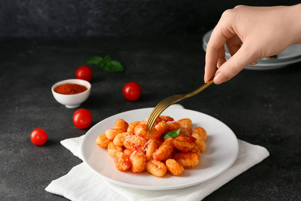 Woman eating delicious gnocchi with tomato sauce on dark background - Photo, Image