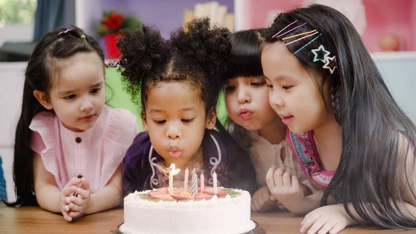 Grupo de niños celebran la fiesta de cumpleaños en el aula, los niños y niñas jóvenes multiétnicos felices de pedir un deseo soplar velas en el pastel de cumpleaños en la escuela. Los niños celebran cumpleaños en el concepto escolar
. - Foto, Imagen