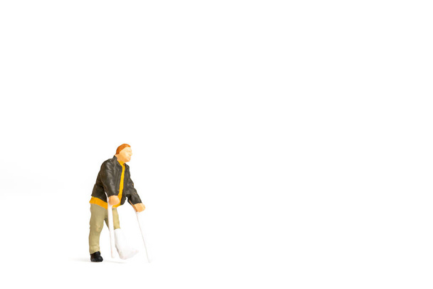 Personas en miniatura, Vista completa de un hombre con la pierna rota está utilizando muleta sobre fondo blanco. - Foto, Imagen