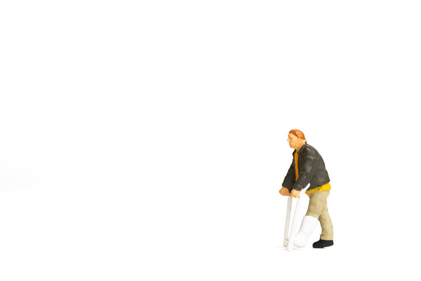 Personas en miniatura, Vista completa de un hombre con la pierna rota está utilizando muleta sobre fondo blanco. - Foto, Imagen