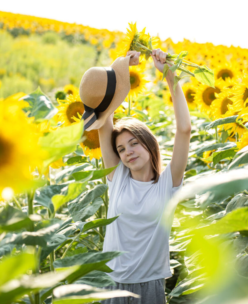 Νεαρή όμορφη κοπέλα περπατά το καλοκαίρι σε ένα χωράφι με ανθισμένα ηλιοτρόπια - Φωτογραφία, εικόνα