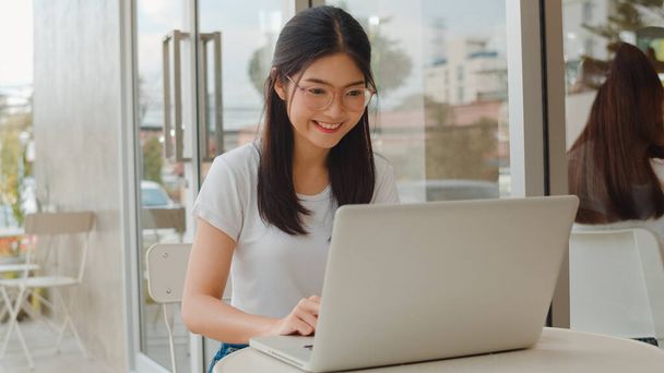 Фріланс азіатські жінки працюють над ноутбуком у кав'ярні. Бізнес-дівчина з Азії, яка використовує комп'ютер для торгівлі, надсилає електронну пошту, цифрову роботу в Інтернеті за столом на відкритому кафе у вечірній концепції. - Фото, зображення