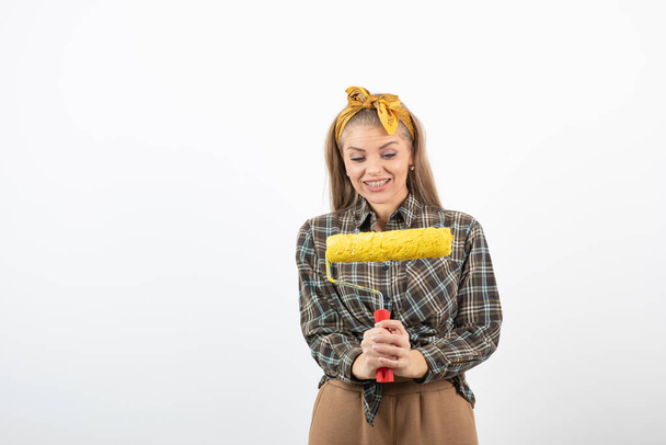 Young blonde woman holding painting roller over a white wall. High quality photo - Foto, imagen
