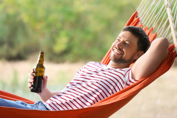 Jovem com garrafa de cerveja deitado na rede ao ar livre - Foto, Imagem