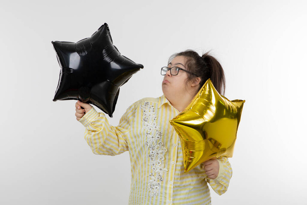 Mädchen mit Down-Syndrom posiert mit goldenen und schwarzen Sternballons - Foto, Bild