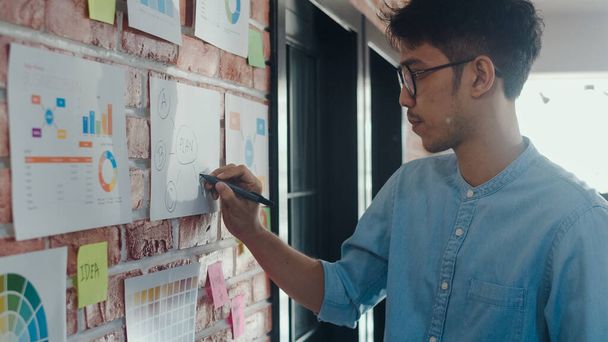 Asijský kreativní muž kreslímá pracovní plán na papírové desce. Mladí profesionální obchodní muži Přemýšlejte a pište si informace na papíře o cihle, obchodní situaci, spuštění v konceptu kanceláře. - Fotografie, Obrázek