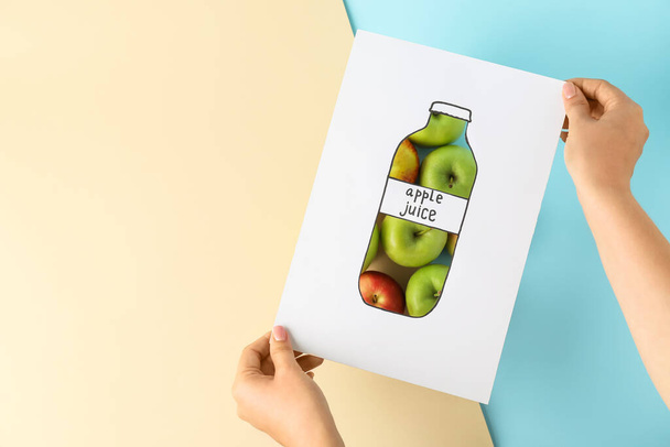 Γυναικεία χέρια με ζωγραφισμένο μπουκάλι χυμό και μήλα στο φόντο χρώμα - Φωτογραφία, εικόνα