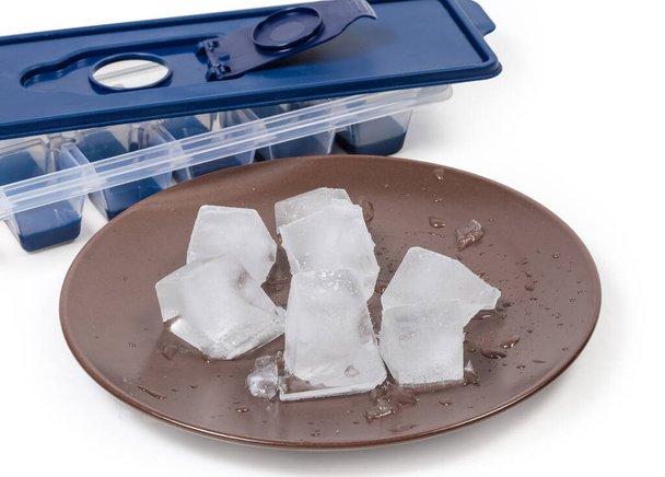 Слегка расплавленные кубики льда на коричневом блюде против плесени для домашнего льда, сделанные на белом фоне, крупным планом в селективном фокусе - Фото, изображение