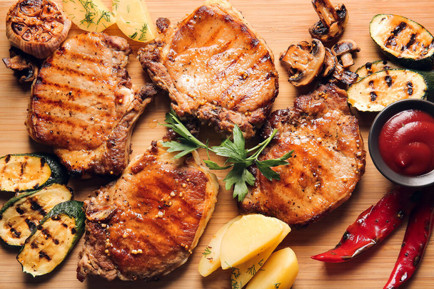 Tasty pork steaks, tomato sauce and grilled vegetables on wooden background - Photo, Image