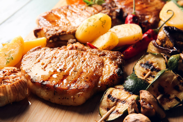Tablero de madera con sabroso filete de cerdo y verduras a la parrilla en la mesa, primer plano - Foto, imagen