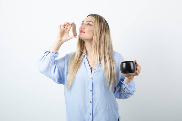 Portrait of young woman holding cup of hot drink and sniffing chocolate bar . High quality photo - Photo, Image