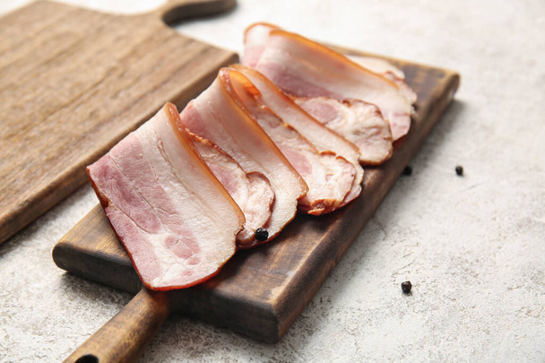 Dřevěná deska s plátky chutné uzené slaniny na světlém pozadí, detailní záběr - Fotografie, Obrázek