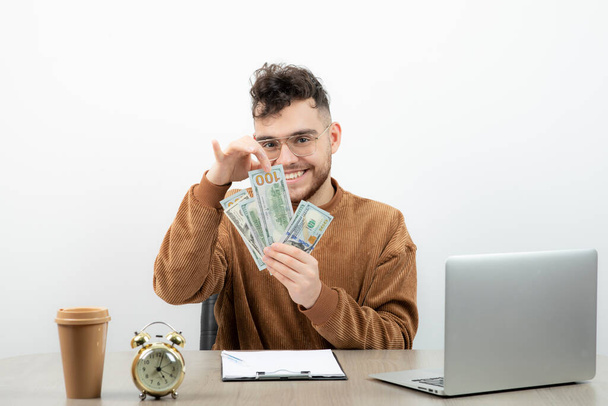 Feliz jovem contabilista sentado em sua mesa e contando dinheiro. Foto de alta qualidade - Foto, Imagem
