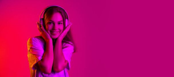 Beautiful young caucasian girl listening to music in headphones isolated on pink background in neon - Photo, Image