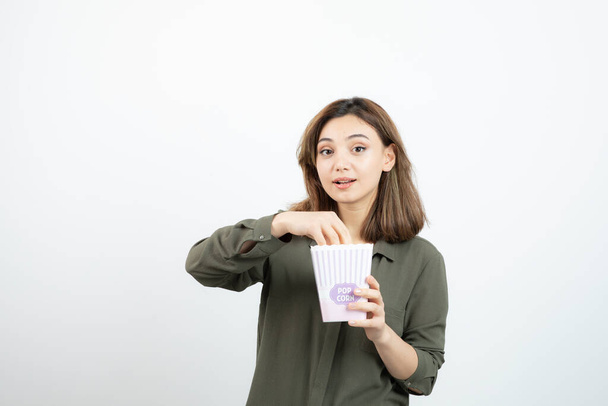 Image d'une jolie fille prenant du pop-corn de la boîte sur un mur blanc. Photo de haute qualité - Photo, image