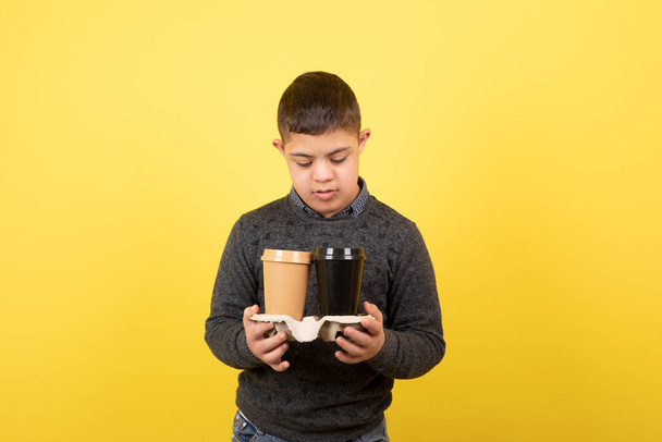 Obraz słodkiego dzieciaka z zespołem Downa patrzącego na filiżanki kawy. Wysokiej jakości zdjęcie - Zdjęcie, obraz