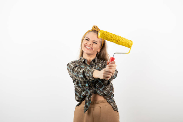 Young blonde woman holding painting roller over a white wall. High quality photo - Fotografie, Obrázek