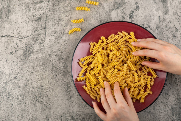 Hands picking raw fusilli pasta on stone background. High quality photo - Foto, afbeelding