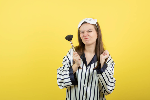 Una hermosa joven en pijama sosteniendo un cepillo contra la pared amarilla. Foto de alta calidad - Foto, Imagen