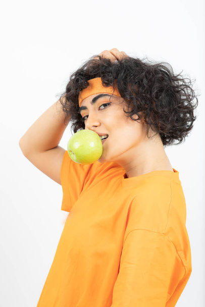 женщина в оранжевой футболке позирует с яблоком - Фото, изображение