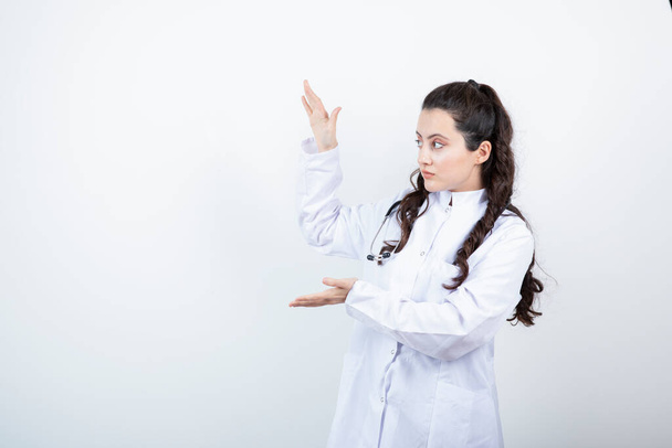 Jeune femme médecin en robe médicale avec stéthoscope montrant les paumes ouvertes. Photo de haute qualité - Photo, image