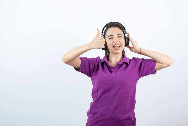 Chica joven escuchando la canción con auriculares y dando pulgares hacia arriba. Foto de alta calidad - Foto, imagen
