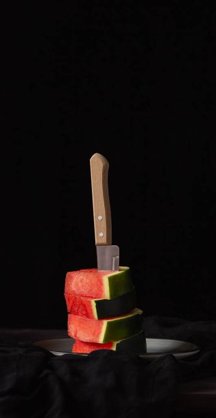 Egy darab görögdinnye fekete háttéren és egy késsel. Rusztikus stílus. - Fotó, kép