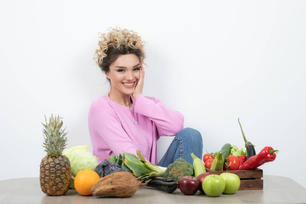 schöne Frau posiert mit verschiedenem Obst und Gemüse auf dem Tisch - Foto, Bild