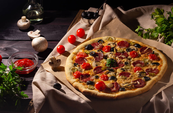 暗い背景にサラミ、キノコ、チェリートマトと自家製ピザ。サイドビュー. - 写真・画像
